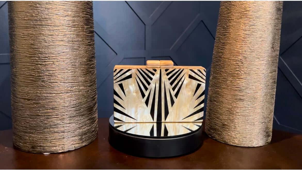 Art deco clutch bag with black and gold geometric design between two textured gold vases