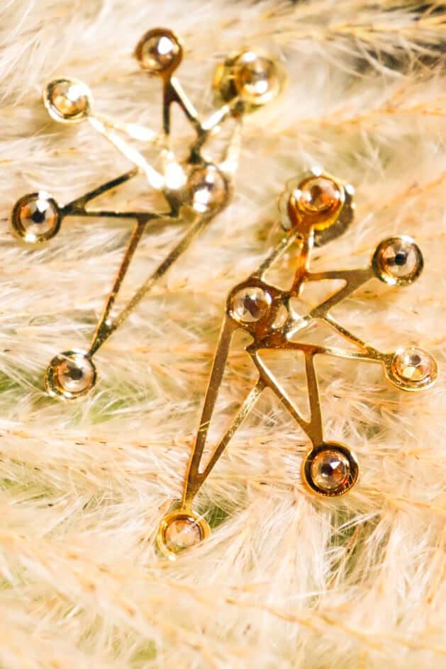 Gold star-shaped earrings with geometric design on soft beige fur background