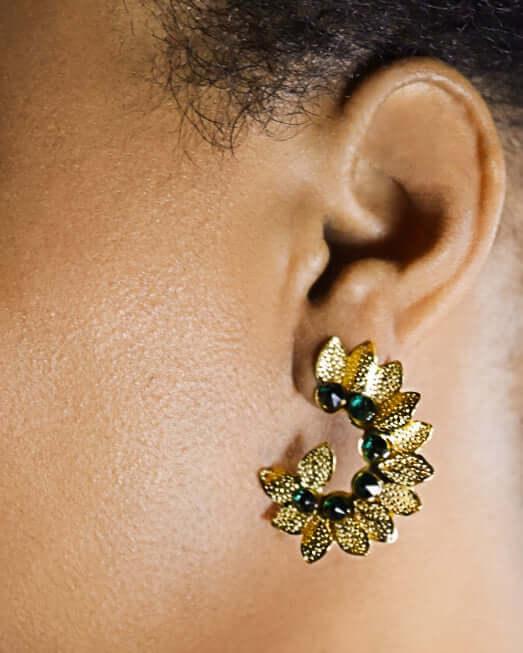 Gold floral hoop earring with green stones on ear, jewelry close-up