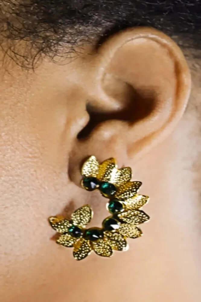 Gold floral wreath earring with green stones on ear, close-up jewelry photo