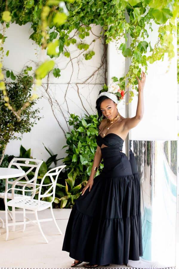Woman in black strapless dress and floral headpiece posing by lush green indoor plants