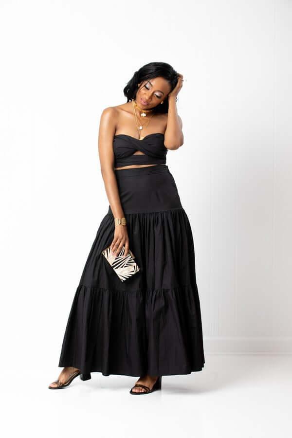 Woman in black strapless crop top and maxi skirt holding patterned clutch bag