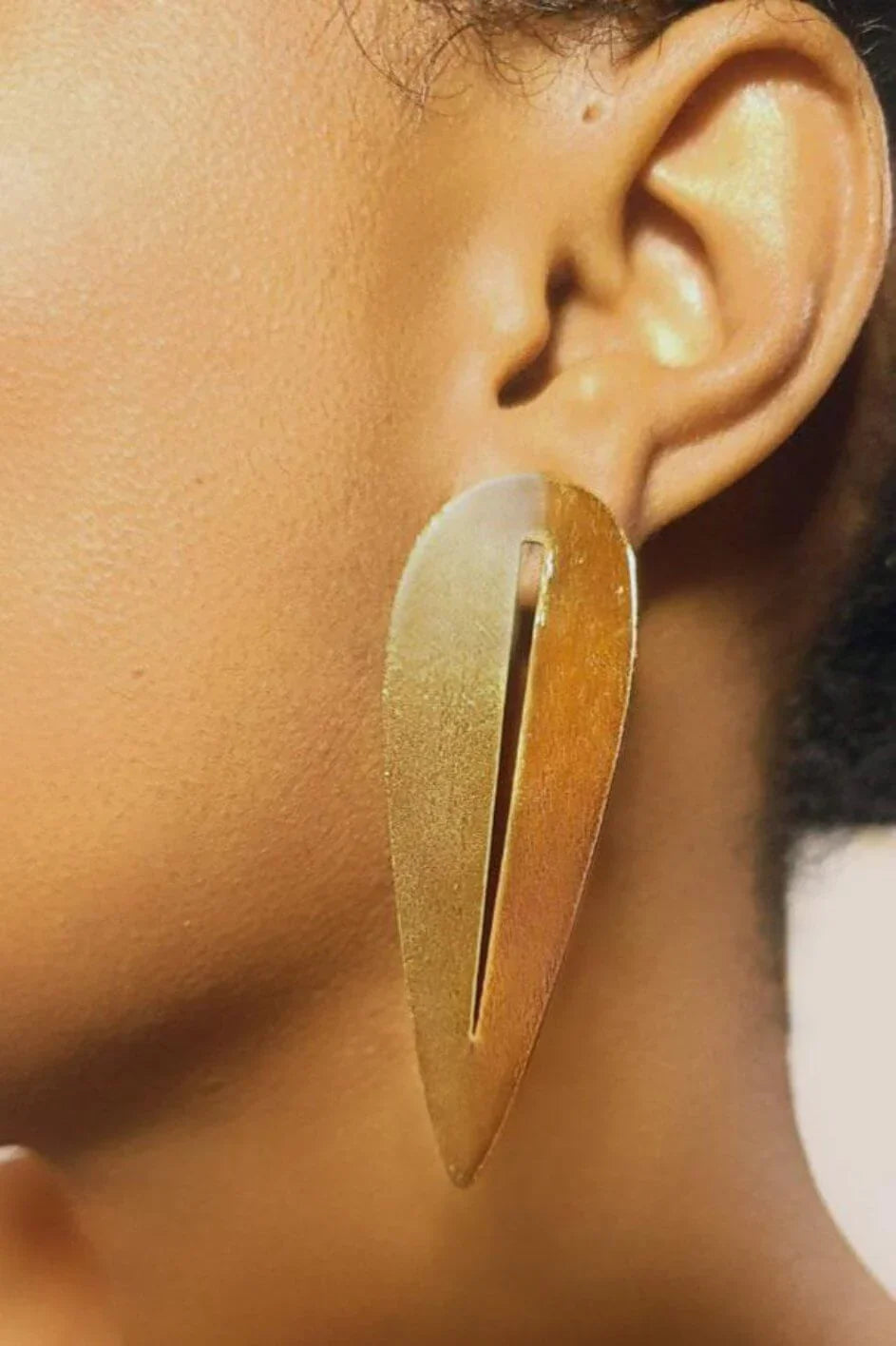 Woman wearing a large gold teardrop statement earring with a geometric cutout