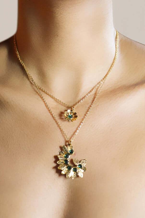 Woman wearing layered gold necklaces with floral pendants and green gemstones